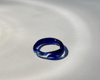 May include: A transparent blue ring with a swirl design. The ring is made of glass and has a rounded shape. The ring is a fashion accessory.