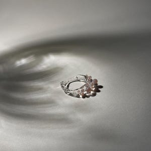 Könnte beinhalten: Ein klarer Glasring mit einer Reihe kleiner rosa Glasperlen um das Band.