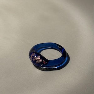 May include: A striking blue glass ring featuring a pink and gold floral pattern. This statement ring is a vibrant accessory, ideal for adding a splash of colour. The ring's distinctive design makes it a unique piece of jewellery.