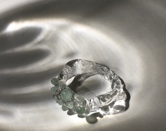 Op de afbeelding: Een ring van helder glas met een cluster van lichtgroene glazen kralen rond de band.