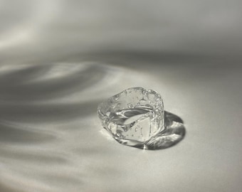 May include: A clear glass ring with a textured surface. The ring is made of glass and has a unique, organic shape.