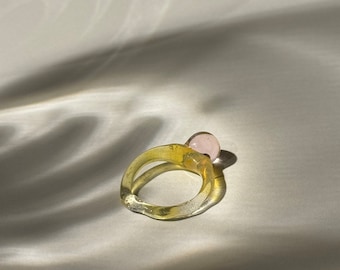 Può includere: Un anello di vetro giallo con una sfera di vetro rosa in cima.