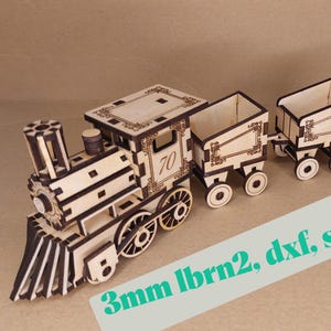 May include: A wooden toy train with a locomotive and two cars. The train is made of light brown wood with dark brown accents. The number "70" is visible on the side of the locomotive. The text "3mm lbrn2, dxf, svg" is on a white rectangle.