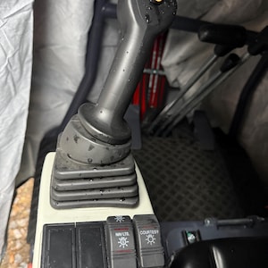 May include: A close-up of a black joystick with a yellow button on top. The joystick is part of a control panel with buttons labeled "NAV LTS" and "COURTESY". The panel is gray and black.