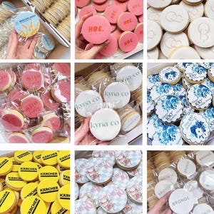 May include: Selection of decorated biscuits with different designs. Some have pink icing with "HBE" text, others feature blue floral patterns, and some display company logos or text such as "Hello Forty" and "Kyria Co."