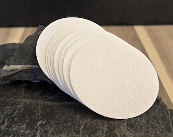 May include: A stack of white round coffee filters, likely for a pour-over coffee maker, on a dark gray stone surface.