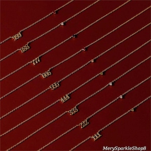 Könnte beinhalten: Ein Satz goldener Halsketten mit verschiedenen Zahlen darauf, jede mit einem kleinen Edelstein-Anhänger. Die Halsketten sind in einer Reihe auf einem roten Hintergrund angeordnet.