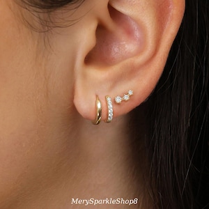 Puede incluir: Primer plano de una oreja adornada con tres pendientes dorados. Uno es un aro simple, otro es un aro con pequeñas piedras transparentes y el tercero es una barra curva con tres piedras transparentes. El texto "MerySparkleShop8" está en la parte inferior.