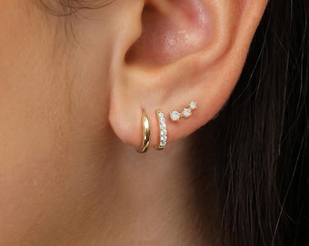 May include: A close-up of an ear adorned with three different gold earrings. One is a simple hoop, another is a hoop with small, clear stones, and the third is a curved bar with three clear stones. The text "MerySparkleShop8" is at the bottom.