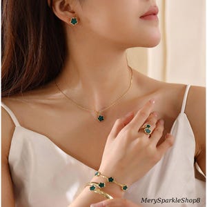 May include: A set of gold-tone jewelry featuring green clover-shaped charms. The set includes a necklace, earrings, a ring, and a bracelet.