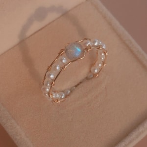 以下が含まれることがあります： 小さな白い真珠で囲まれた大きな虹色の宝石が付いた金の指輪