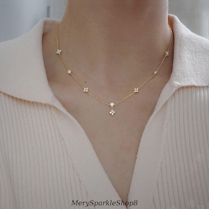 Könnte beinhalten: Eine zarte goldene Halskette mit einem kleinen Anhänger, der mit einer Gruppe von klaren Zirkonia-Steinen besetzt ist. Die Halskette ist mit kleineren Zirkonia-Steinen in einem Blumenmuster verziert.