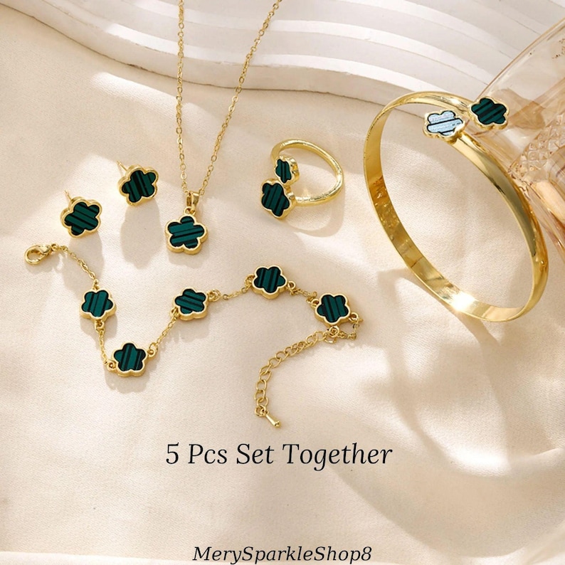 May include: A 5-piece jewelry set featuring a gold necklace, bracelet, ring, and earrings. Each piece has a green clover-shaped pendant with a gold border.