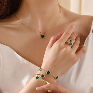 May include: A gold necklace with a green clover pendant, a gold ring with two green clover stones, and a gold bracelet with five green clover charms.