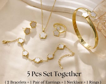 May include: A gold-toned jewelry set featuring a necklace, ring, earrings, and two bracelets. Each piece has a flower-shaped design with a white center. The text "5 Pcs Set Together" is visible.