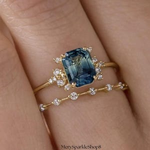 Peut inclure: Un ensemble de bagues de fiançailles en or, comprenant une grande pierre précieuse rectangulaire de couleur teal. La bague principale est ornée de petits diamants transparents. Une fine alliance avec de petits diamants transparents complète la bague principale.