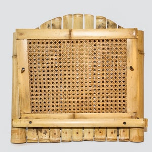 Può includere: Un ripiano a parete in bambù naturale intrecciato con un'apertura rettangolare e un pannello in canna intrecciato. Il ripiano ha una parte superiore arcuata decorativa con più pezzi di bambù.