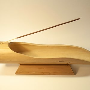 Può includere: Un porta incenso in bambù naturale con un design curvo e una base in legno. Un bastoncino di incenso è posto nel porta incenso.