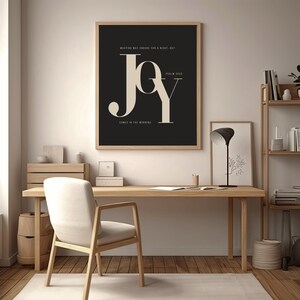 May include: A framed print featuring the word "JOY" in large, stylish lettering on a black backdrop. The print also includes the text "WEEPING MAY ENDURE FOR A NIGHT, BUT COMES IN THE MORNING." The frame is a light wood colour.