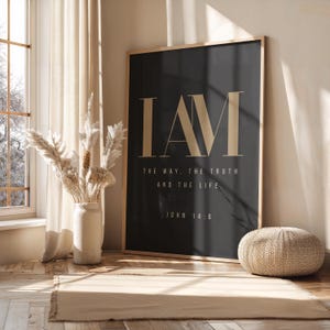 Puede incluir: Un gran cuadro rectangular enmarcado con fondo gris oscuro y letras de color beige claro. El texto dice I AM THE WAY, THE TRUTH AND THE LIFE. JOHN 14:6 en una fuente serif moderna y limpia. El marco es de madera natural de tono claro.