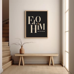 May include: A rectangular wall art print in a light wood frame featuring a black background with the beige text ELO HIM and the smaller text GOD THE CREATOR centered below. The typography is serif and bold with a small beige dot between the words.