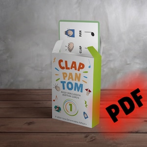May include: A white rectangular box of Clap Pan Tom body percussion rhythm cards with colourful text and illustrations. The box features a green side panel and a card extending from the top showing a hand icon, the word PAN, and a musical note.