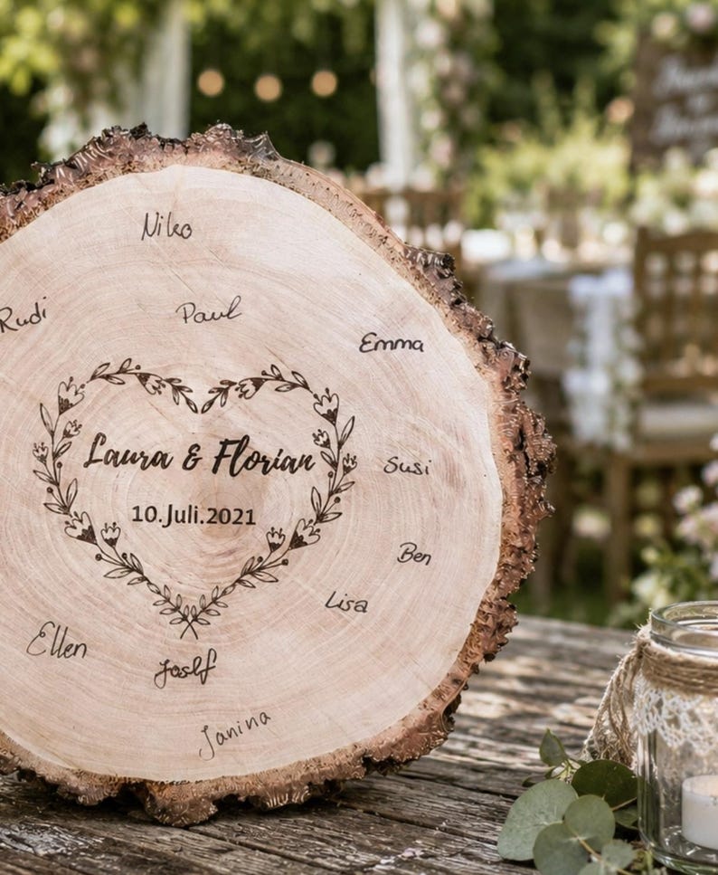 May include: A rustic wooden wedding sign with a natural bark edge. The sign is engraved with the names "Laura & Florian" inside a floral heart, along with the date "10. Juli.2021". Names of guests are written around the edge.