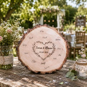 May include: A rustic wooden wedding sign with a natural edge. The sign features a heart-shaped design with the names "Laura & Florian" and the date "10. Juli.2021" in the center, surrounded by guest names. The sign is displayed on a wooden table.