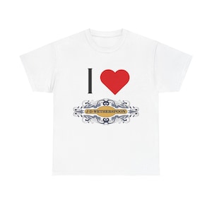 Puede incluir: Camiseta blanca con un diseño gráfico. El diseño presenta una línea vertical negra, un corazón rojo y el texto "J.D. Wetherspoon" en un óvalo decorativo. Una prenda informal.