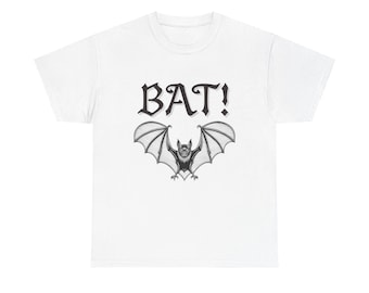 May include: White t-shirt featuring a black and white illustration of a bat with outstretched wings. Above the bat is the word "BAT!" in a bold, stylized font. The design is centered on the shirt, creating a striking visual.