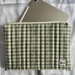 May include: A green and white gingham-patterned tablet sleeve with a zip closure. The sleeve is quilted and has a small white label with the word "Nalu". A tablet and stylus are partially visible inside the sleeve.