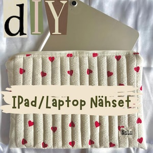 May include: DIY iPad/Laptop Sewing Kit - A white fabric case with red hearts printed on it. The case has a zipper closure and is designed to fit an iPad or laptop. The case is shown with a tablet inside. The text "DIY iPad/Laptop Nähset" is written on the case. The text "Nalu" is also visible on the case.