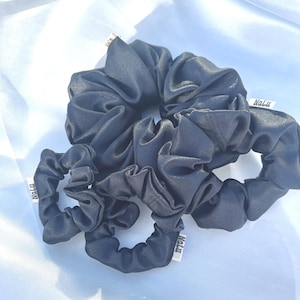 Könnte beinhalten: Vier schwarze Satin-Haargummis mit dem Wort "Nalu" auf dem Stoff.