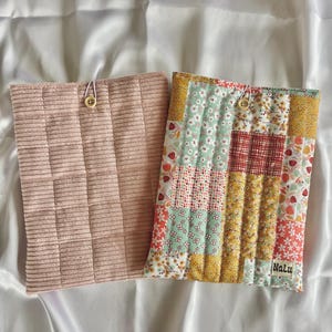 以下が含まれることがあります： ボタンと留め具のループが付いた布製のポーチが2つ。1つのポーチはピンクでリブの質感。もう1つのポーチは、黄色、緑、赤、白の花柄の生地を組み合わせたパッチワークで、右下に「Nalu」という文字が印刷されています。