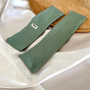 Könnte beinhalten: Zwei Kopfbänder aus Salbeigrün, eines mit einem kleinen weißen Etikett mit der Aufschrift "Nalu".