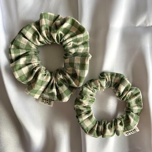 May include: Two green and white gingham scrunchies with the word "NOLA" printed on the fabric.