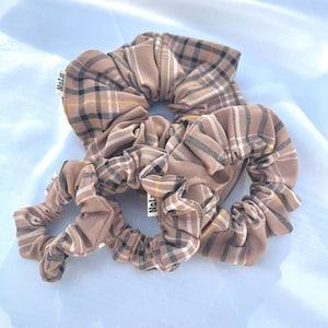 May include: Three brown and white plaid scrunchies with the word "Nalu" printed on two of them.