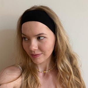 Könnte beinhalten: Eine Frau mit langen blonden Haaren trägt ein schwarzes Stirnband und eine zarte Halskette mit Blumenform.