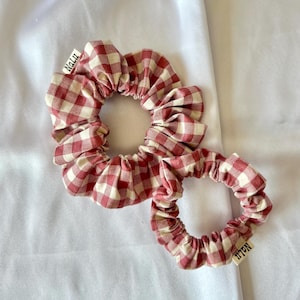 Könnte beinhalten: Zwei rote und weiße Gingham-Scrunchies mit dem Wort "Nalu" auf dem Stoff.