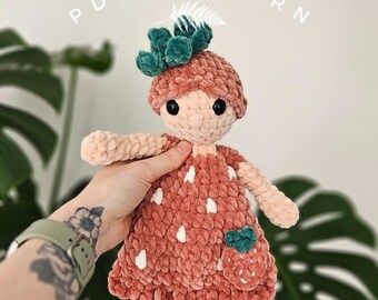 Puede incluir: Muñeca de ganchillo hecha a mano con forma de fresa. La muñeca tiene un cuerpo rosa con lunares blancos, una corona de hojas verdes y un pequeño bolsillo de fresa. El texto "PDF PATTERN" es visible en el fondo.