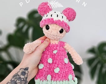 Puede incluir: Muñeca de ganchillo hecha a mano con un vestido rosa y un sombrero blanco y rosa. La muñeca tiene un tono de piel claro, ojos negros y una expresión sonriente. El vestido presenta lunares verde claro y un ribete verde claro. El texto "PDF PATTERN" está arriba.