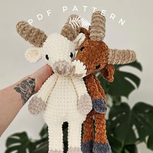 Puede incluir: Dos animales de peluche tejidos a crochet, uno marrón y otro blanco, con patas y orejas largas. El animal marrón tiene una nariz y pezuñas grises. El animal blanco tiene una nariz y pezuñas beige. Los animales están unidos por una mano.