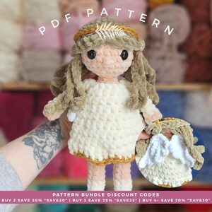 May include: A handmade crochet doll with a cream-colored dress, tan hair, and a gold headband with a fern. The doll has black eyes and pink cheeks. The text "PDF PATTERN" is at the top. The doll is held in a hand.