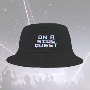Könnte beinhalten: Schwarzer Bucket Hat mit dem Text "ON A SIDE QUEST" in einer verpixelten, verzerrten Schriftart.