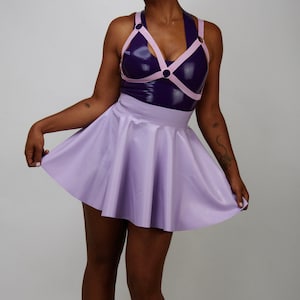 May include: A woman wearing a purple and pink latex top with a matching lavender skirt. She is wearing black platform shoes and has her hair pulled back in two buns.