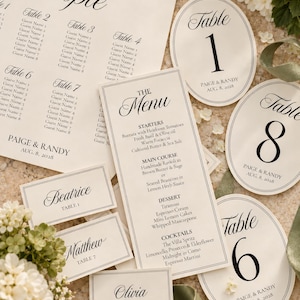 May include: A wedding stationery set featuring a seating chart, a menu, oval table numbers, and rectangular place cards. The cream-colored paper has black serif and script text, including names like Paige and Randy, and dates of Aug. 8, 2028.