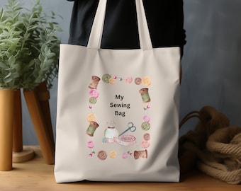 Pode incluir: Uma bolsa tote de lona branca com um design de suprimentos de costura, incluindo carretéis de linha, botões, agulhas e uma fita métrica. O texto "My Sewing Bag" é impresso em preto na bolsa.