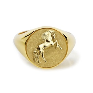 Puede incluir: Un anillo de sello de oro con una imagen en relieve de un caballo en la cara del anillo.