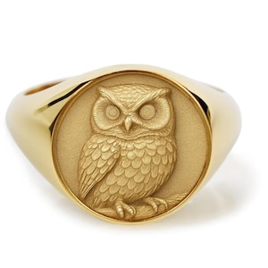 May include: A gold signet ring featuring a detailed relief of an owl. The owl is centered on a circular face, with a polished gold band. The ring's design is classic and elegant, suitable for everyday wear or special occasions.