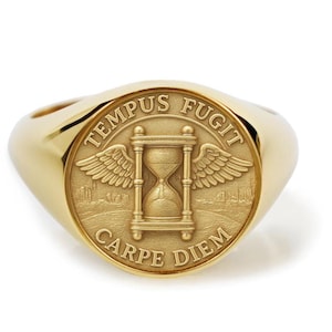 May include: A gold signet ring with a circular face. The face displays an hourglass with wings, and the Latin phrases "TEMPUS FUGIT" and "CARPE DIEM" are inscribed around it. The ring has a polished, reflective surface and a classic design.
